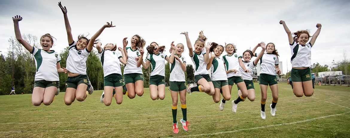 Alumnas de Primaria saltan con los brazos en alto en el campo de deportes
