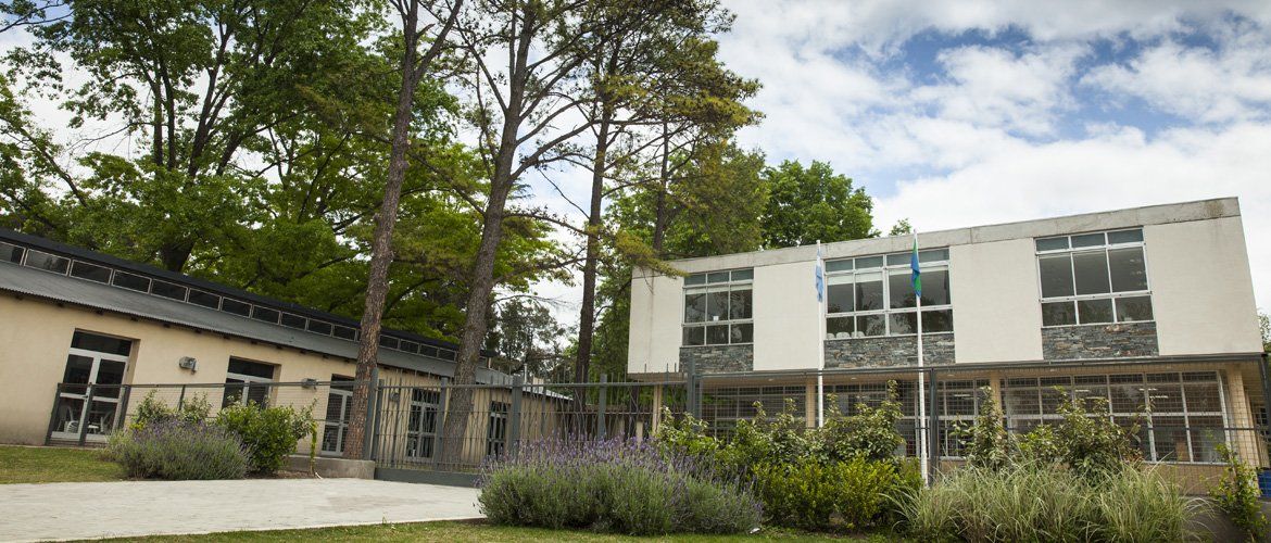 Edificio de la sede Haras Santa María entre árboles, con el campo de deportes al frente