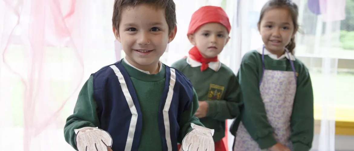 Tres chicos de Nivel Inicial con el buzo verde del colegio sonríen a cámara