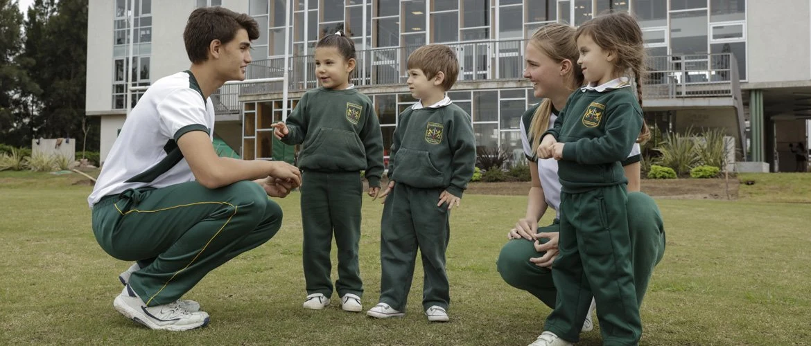 Dos alumnos de Secundaria en cuclillas junto a tres chicos de Nivel Inicial, frente al edificio de la sede Nordelta