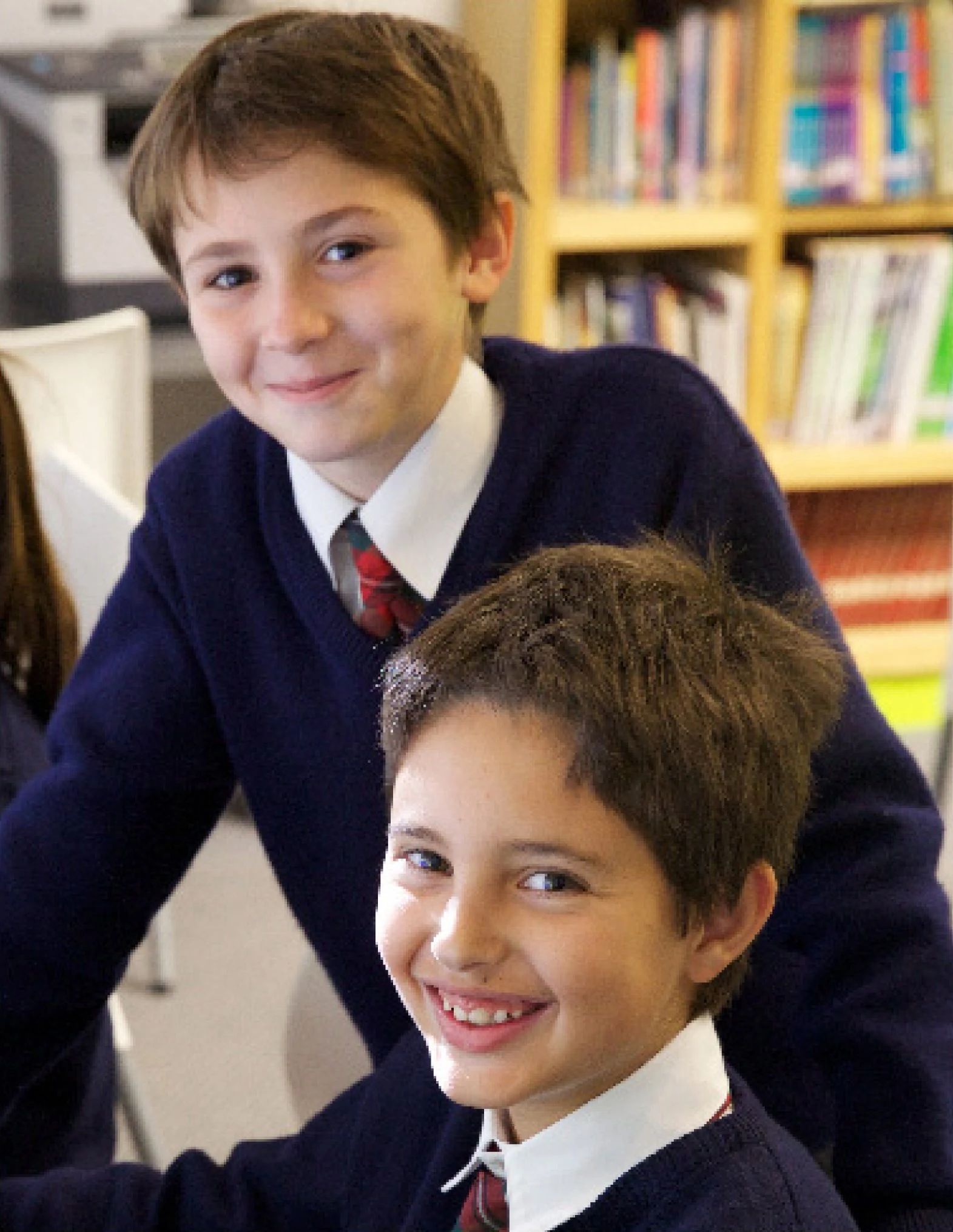 Dos alumnos de Primaria sonríen entre los estantes de la biblioteca