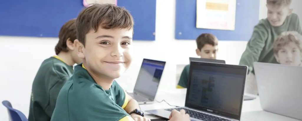 Un alumno de Primaria sonríe frente a su notebook en la clase de programación