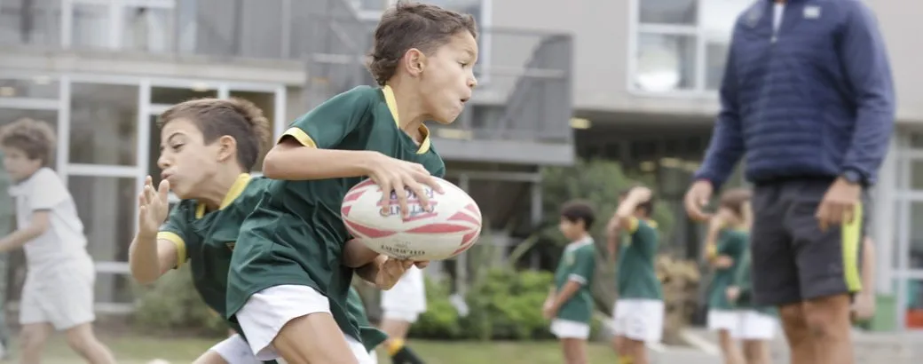 Dos chicos de Primaria corren con la pelota en un partido de rugby